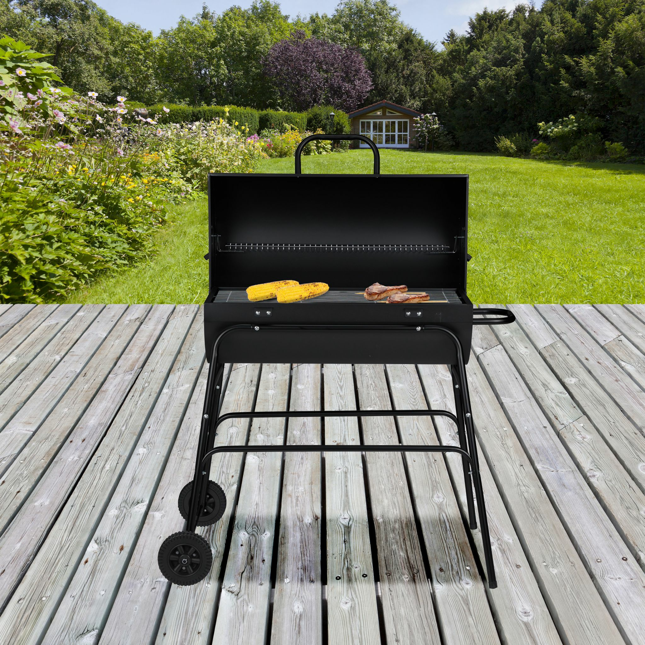 Ein schwarzer Holzkohlegrill mit Maiskolben und Fleisch auf einem Holzdeck im Garten.