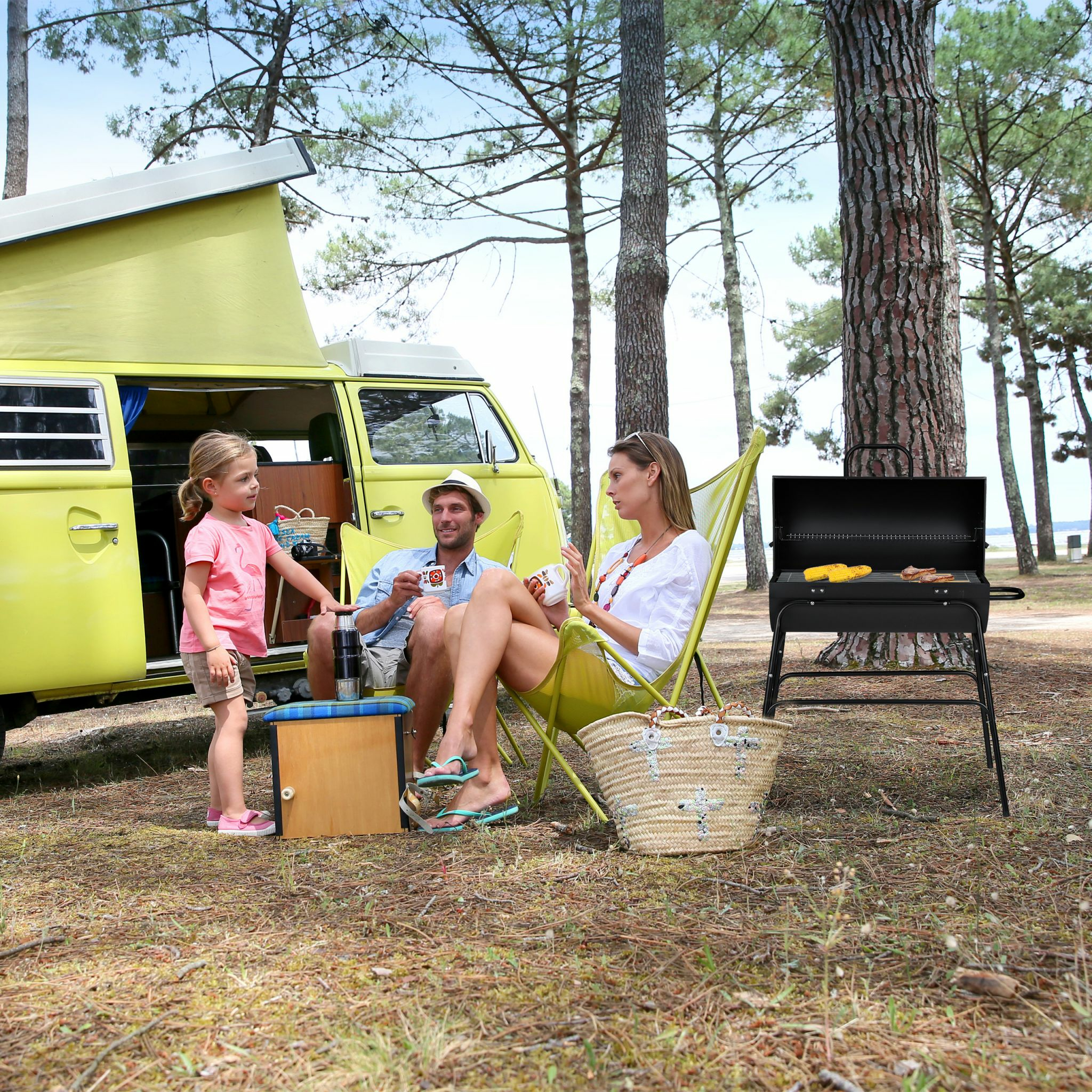 Familie campen im Wald neben einem gelben Wohnmobil mit Grill.