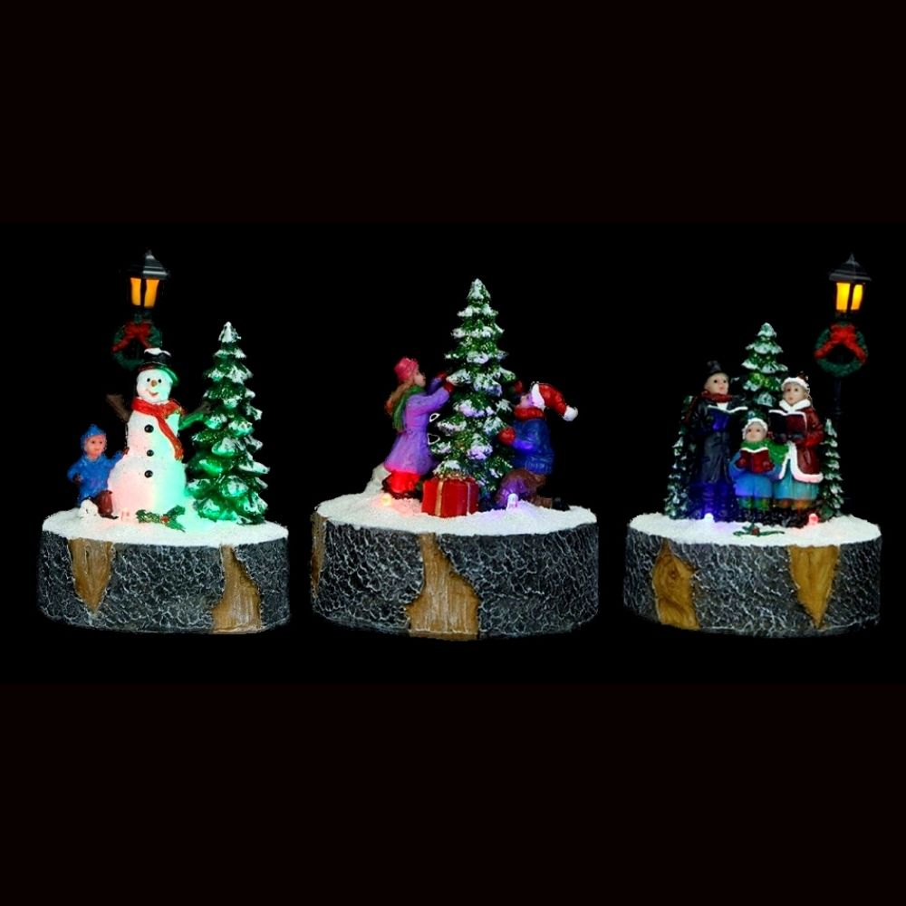 Tres dioramas navideños invernales sobre bases de troncos muestran a niños con un muñeco de nieve y un árbol.