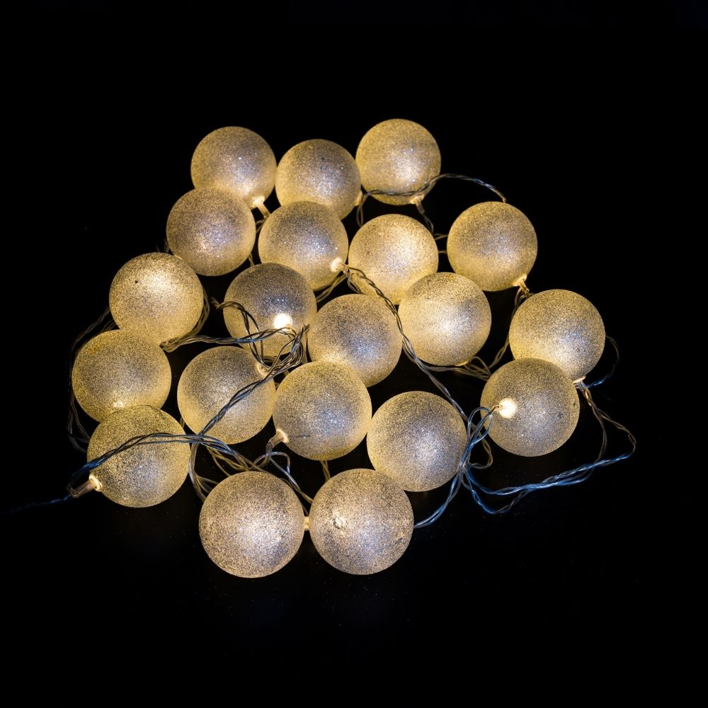 Un grupo de luces de cadena esféricas blancas brillantes y relucientes sobre un fondo oscuro.