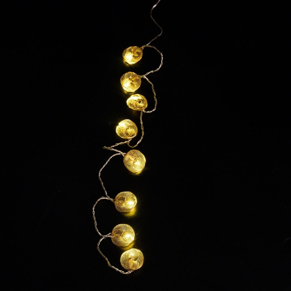 Una cadena de luces con esferas de alambre dorado brilla cálidamente sobre fondo negro.