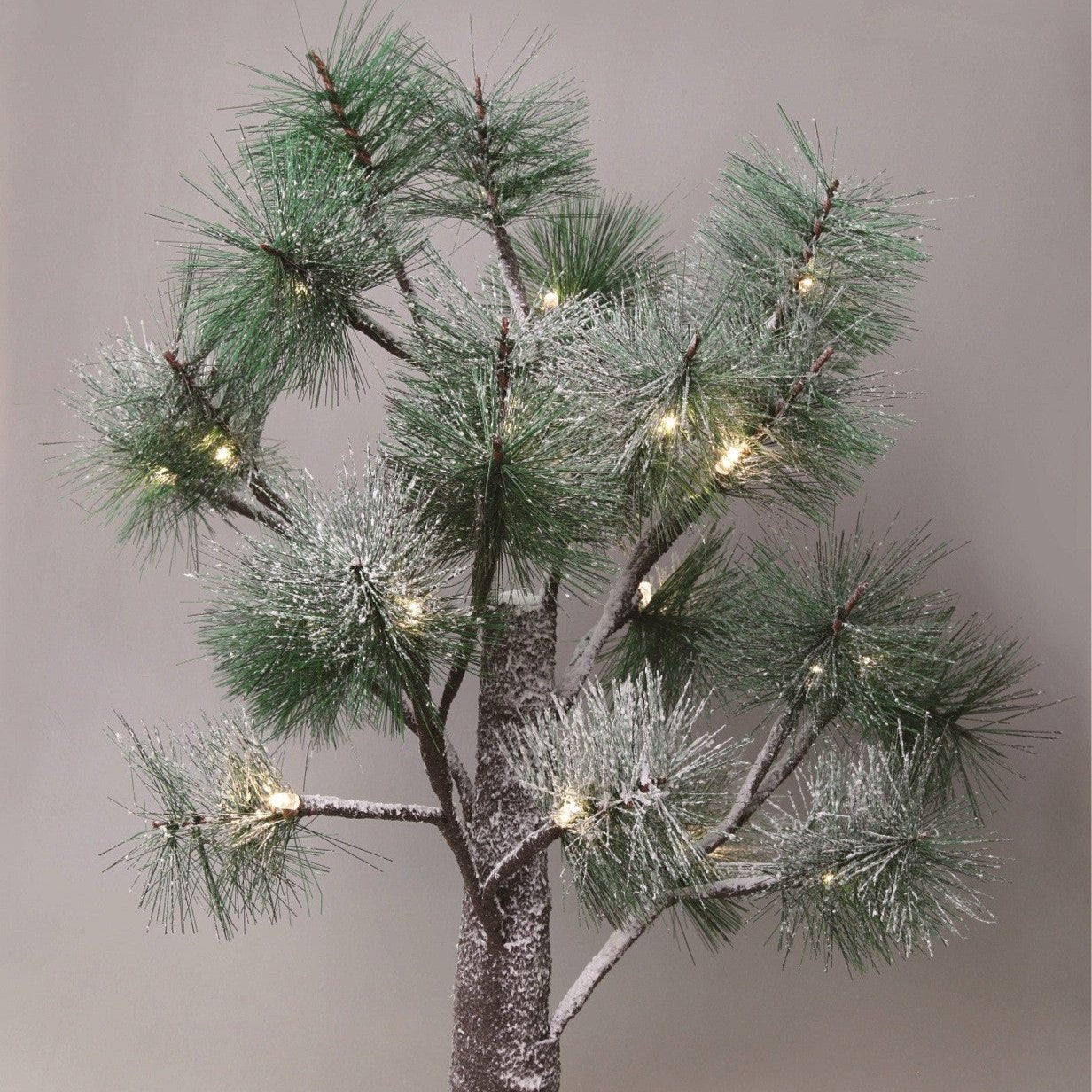 Un pino artificial con nieve en las ramas y luces cálidas sobre un fondo gris.
