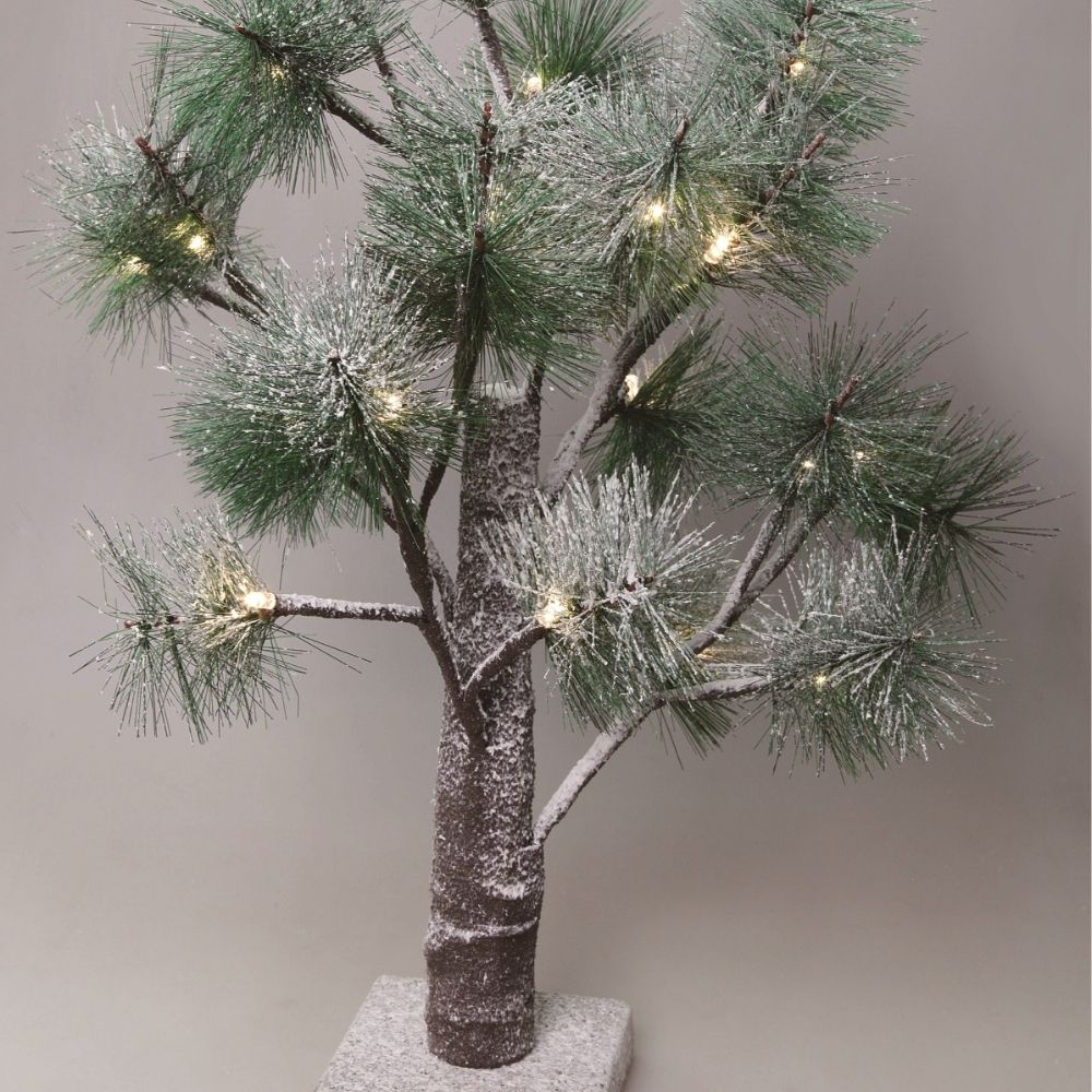 Un pino artificial de mesa nevado con luces cálidas sobre un fondo gris liso.