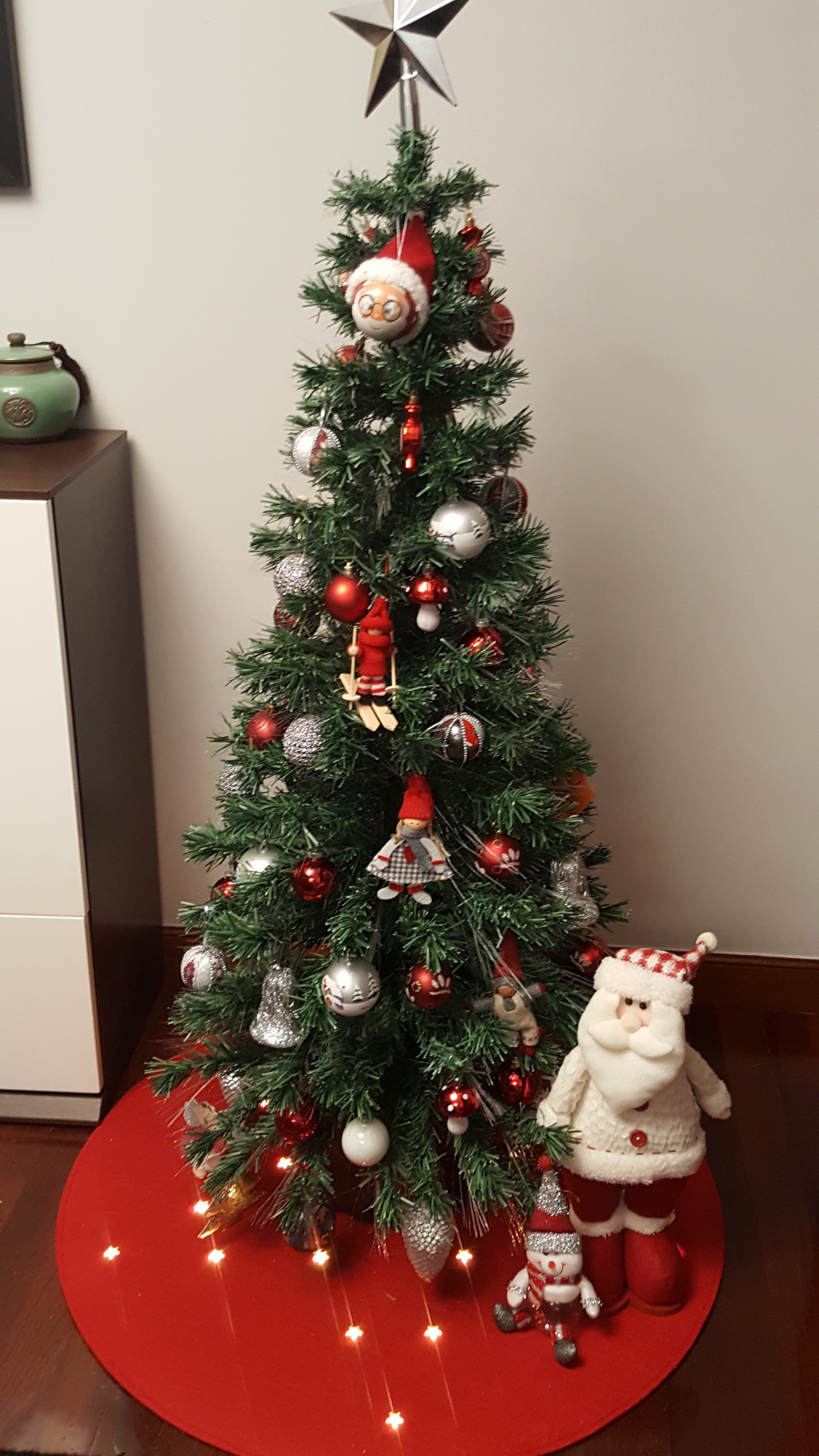 Un árbol de Navidad decorado con estrella, adornos rojos y plateados, y un peluche de Santa Claus.