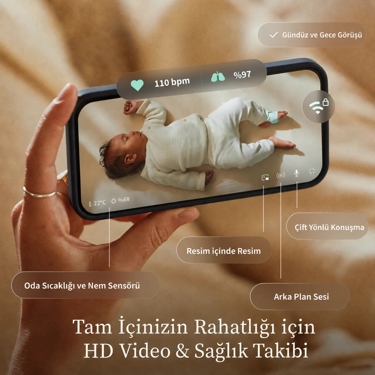 Bir el, bebek monitörü uygulaması gösteren bir telefonu tutuyor; vitaller ve oda sıcaklığı var.