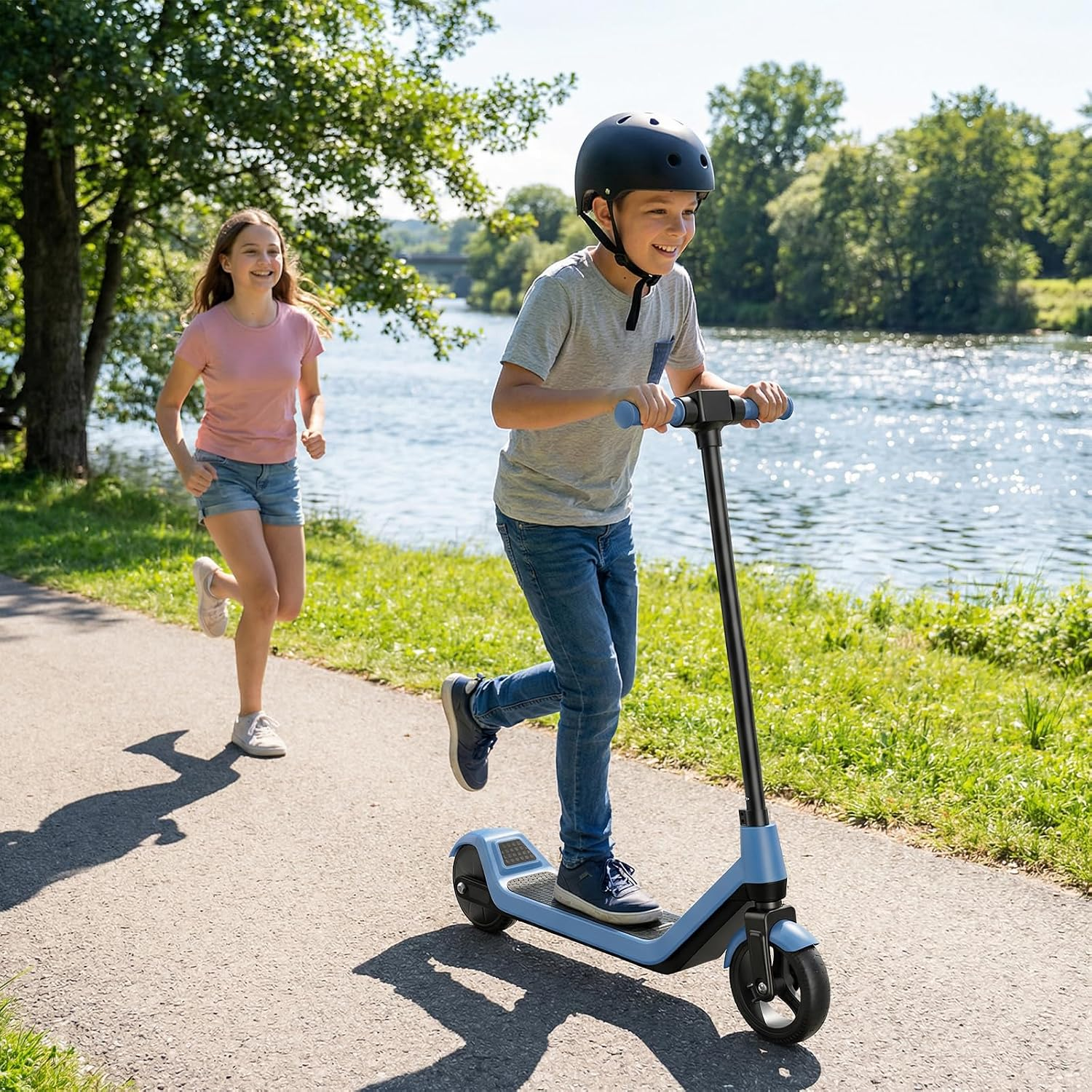 Ein Junge fährt auf einem blauen E-Scooter auf einem Weg am Fluss, während ein Mädchen neben ihm herläuft.