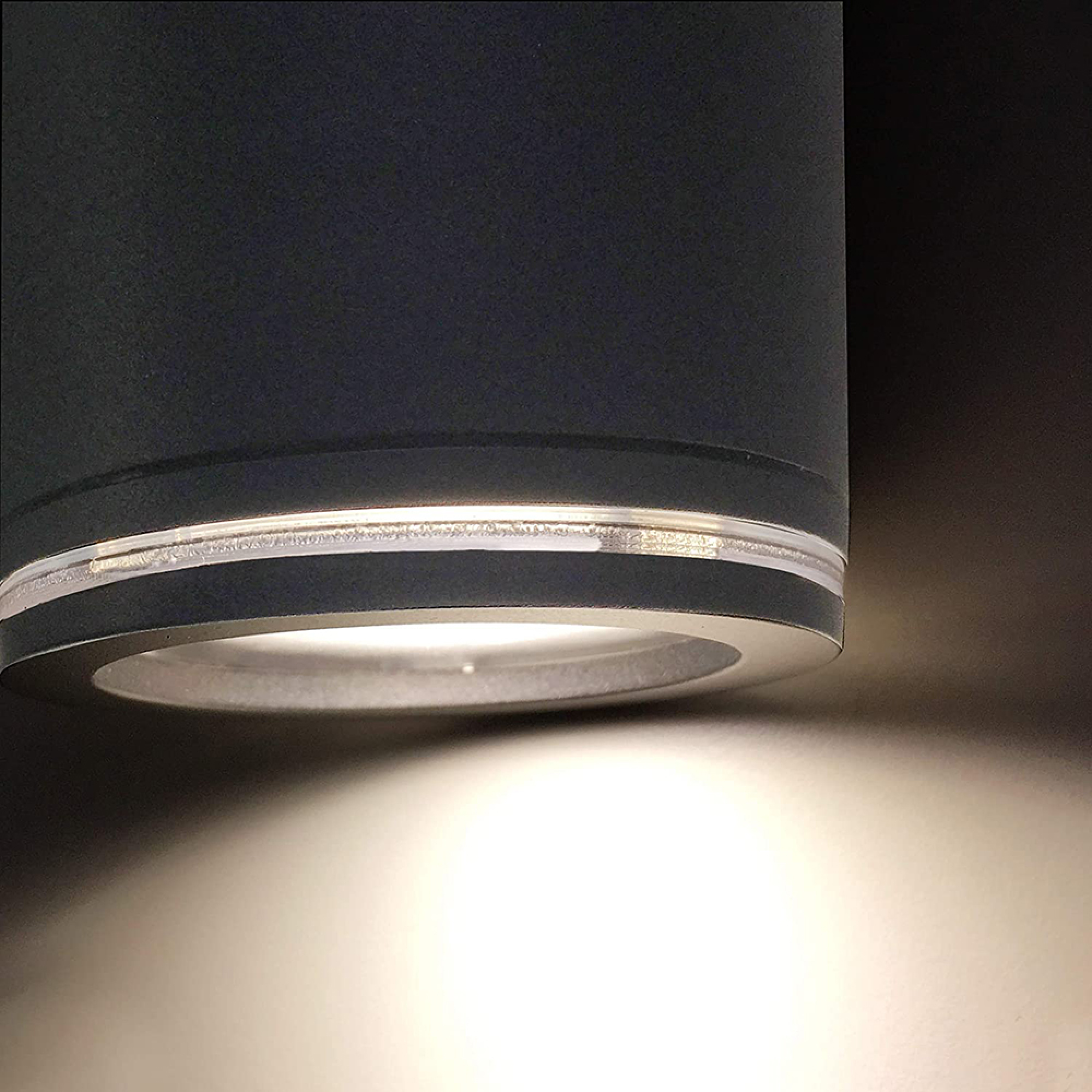 Ein schwarzer zylindrischer Strahler wirft helles Licht nach unten an eine dunkle Wand.
