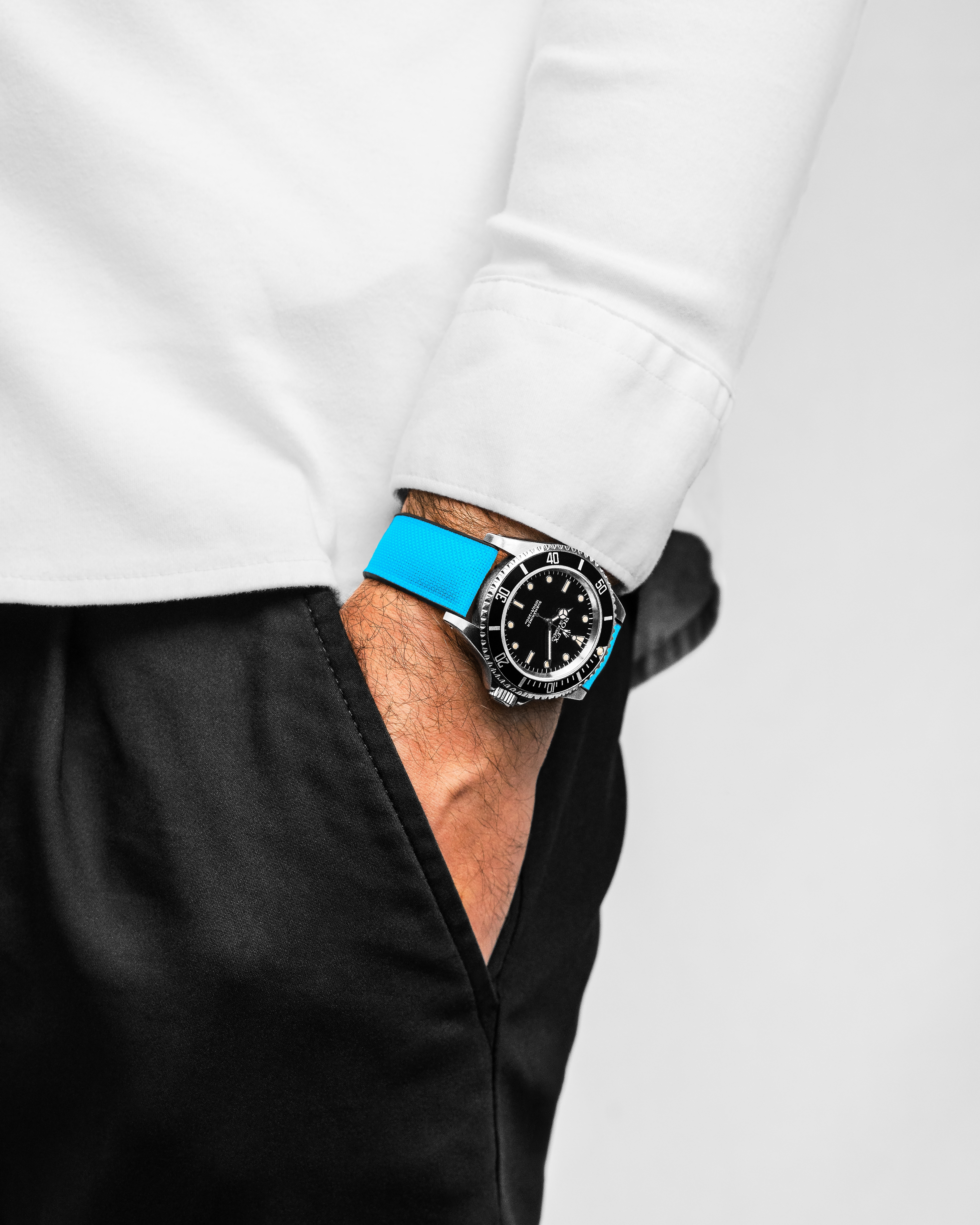 Armbanduhr mit blauem Armband an einem Arm in weißem Hemd.