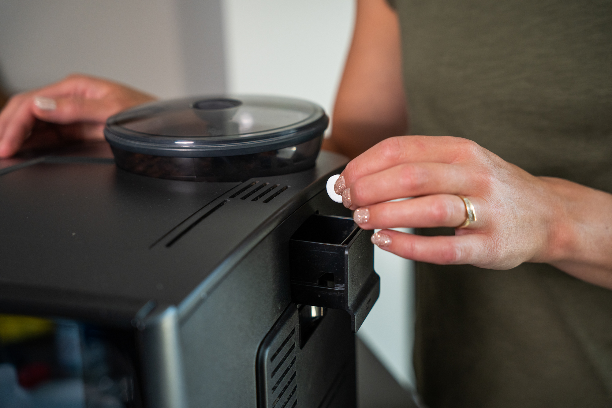 A woman places a cleaning tablet into the compartment of a black coffee machine.