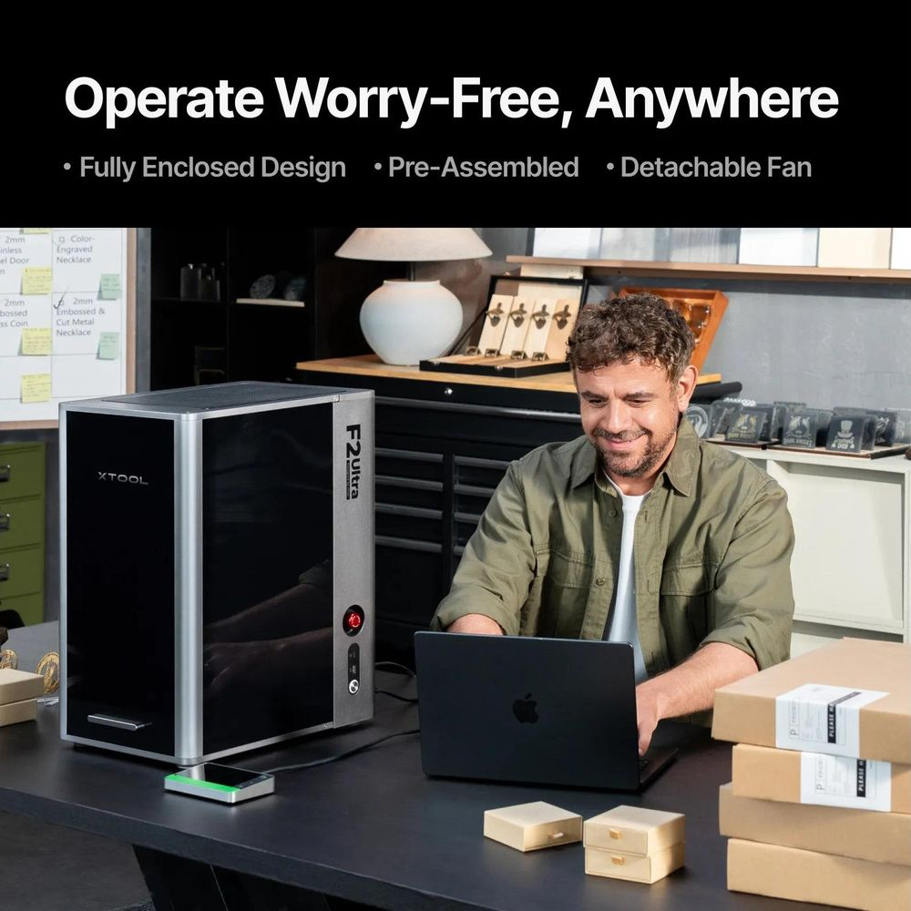 Un uomo seduto a una scrivania usa un laptop vicino a una macchina laser xTool F2 Ultra.
