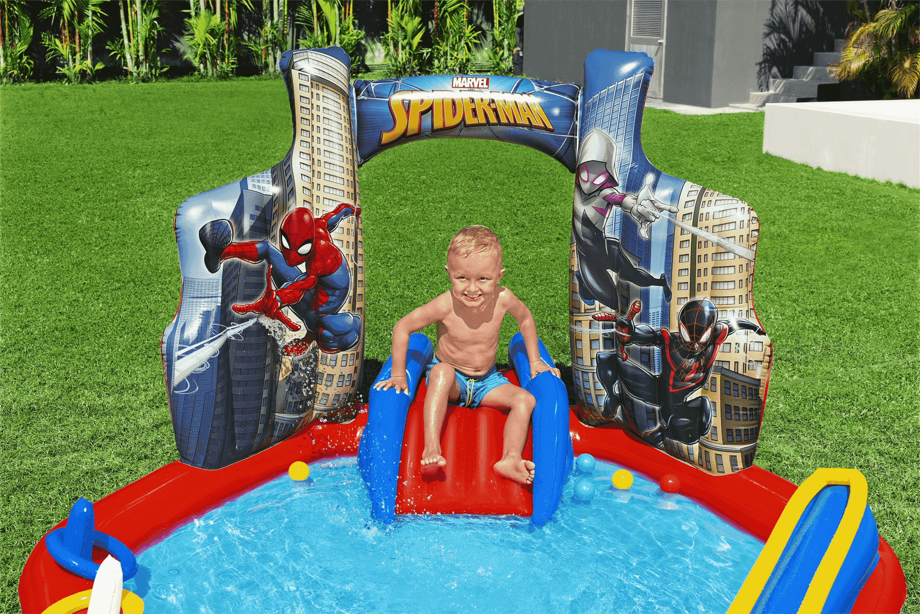 Un niño pequeño se desliza en una piscina inflable de Spider-Man con tobogán.