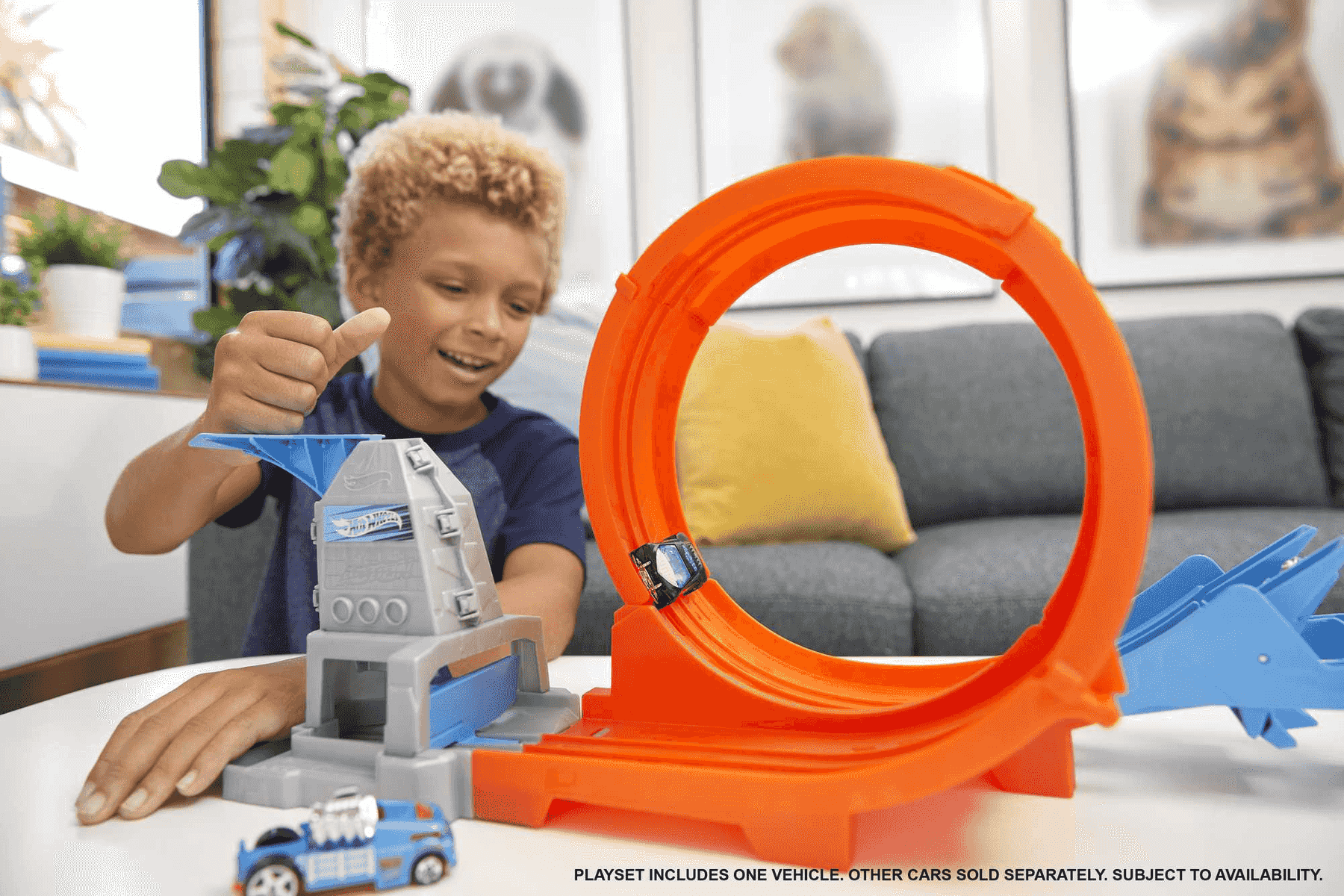 Un niño juega felizmente con un gran circuito de carreras de juguete naranja con un coche pequeño.
