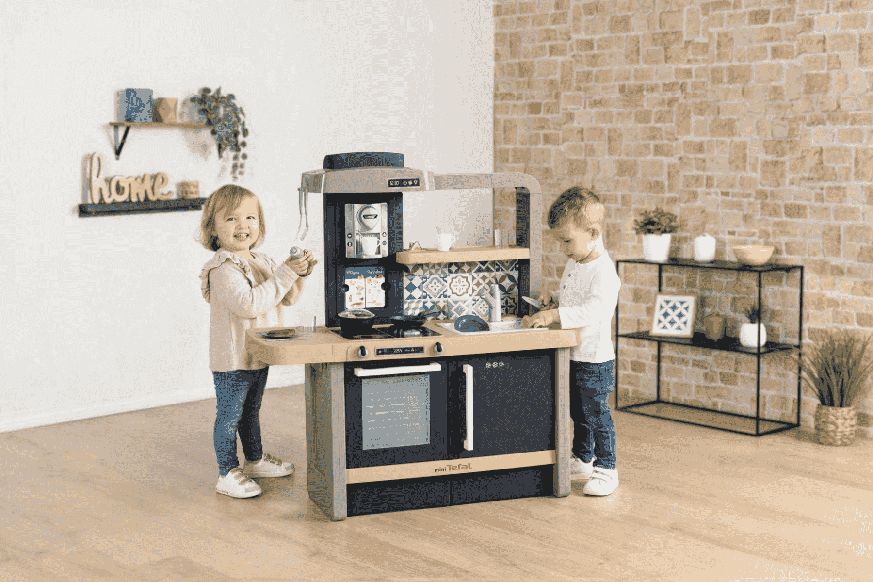 Dos niños pequeños juegan juntos con una cocina de juguete moderna en una habitación luminosa con suelo de madera.
