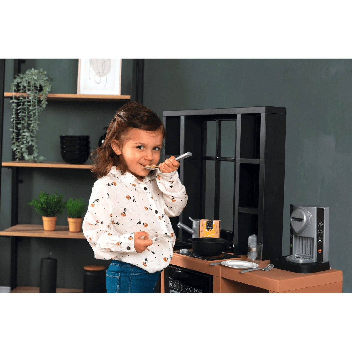 Una niña jugando con una cocina de juguete, sosteniendo una cuchara frente a un estante.