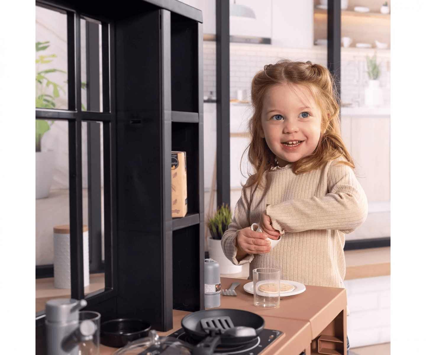 Una niña sonriente juega con una cocina de juguete en un espacio luminoso.