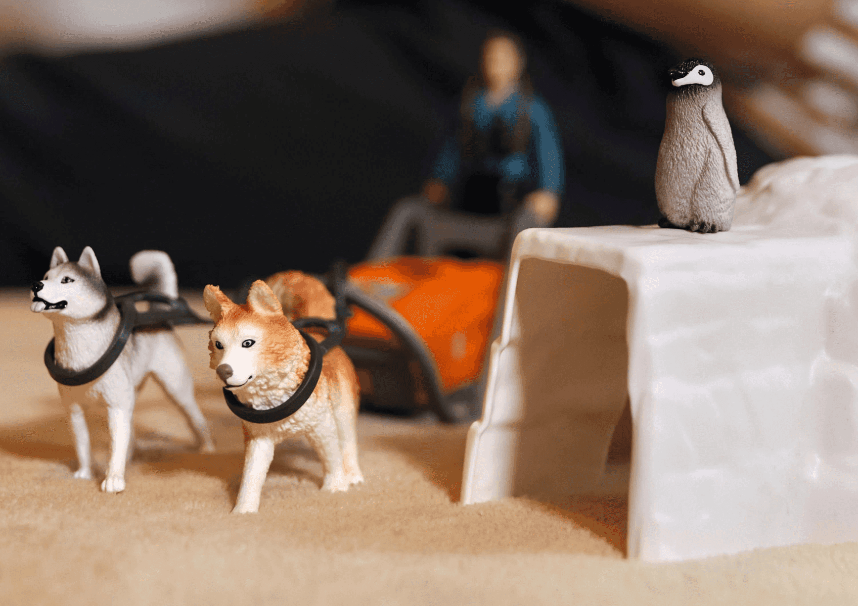 Perros de trineo de juguete tiran de un trineo con un pingüino en un saliente helado.
