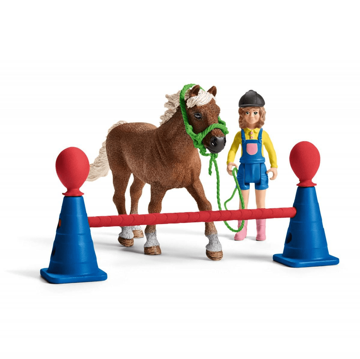 Eine Spielzeugfigur eines braunen Ponys mit grünem Halfter und Reiterin neben blauen Pylonen und roter Stange.