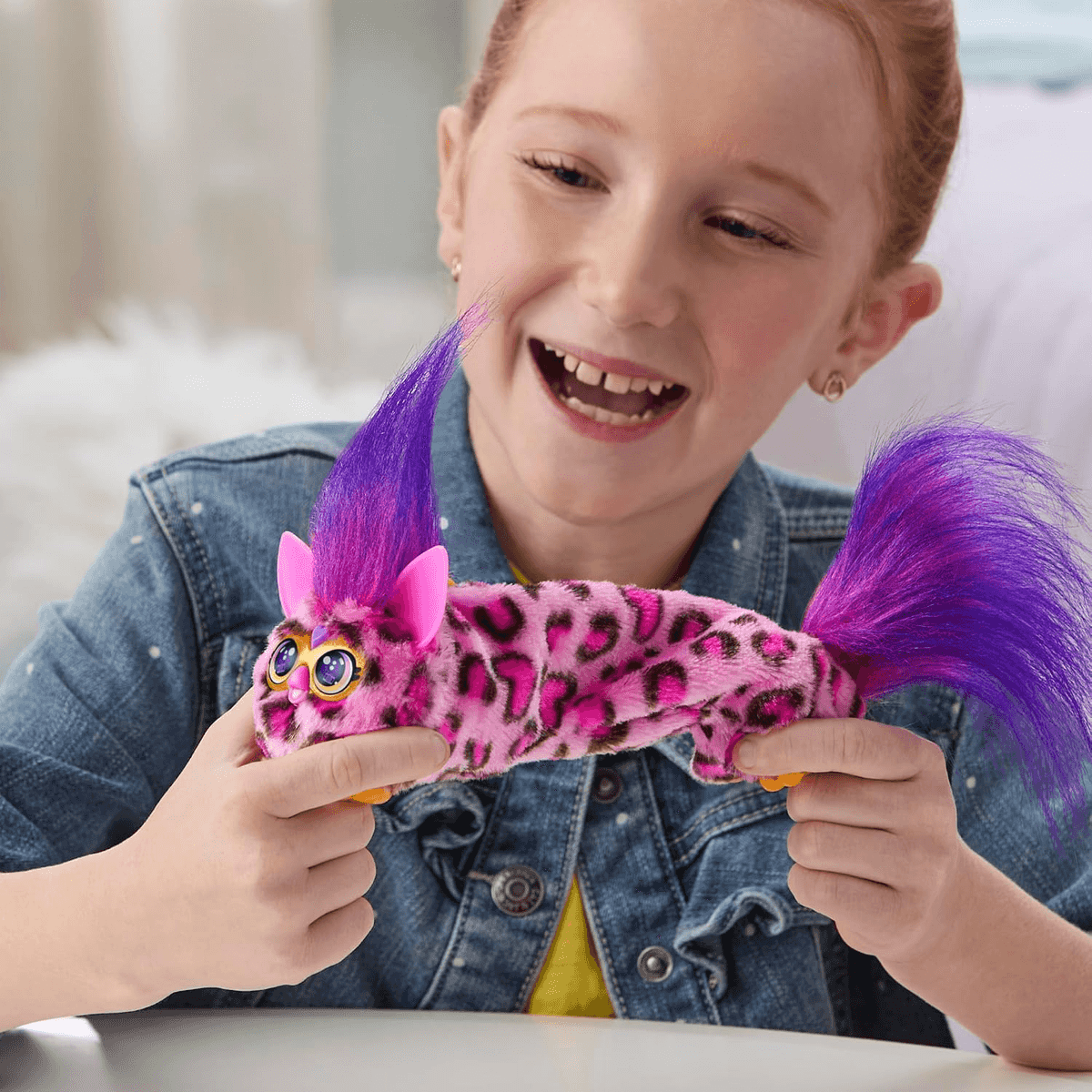 Una niña feliz con camisa de mezclilla sostiene un peluche rosa con pelo morado.
