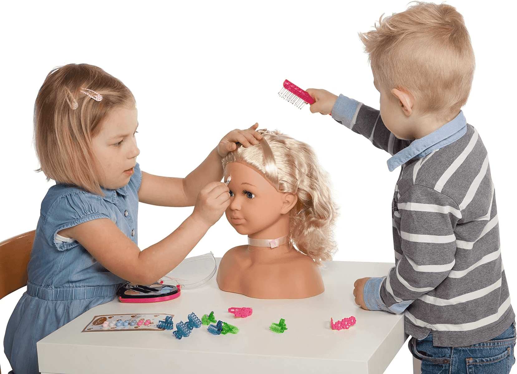 Ein Junge und ein Mädchen stylen gemeinsam den Kopf einer Spielpuppe auf einem weißen Tisch.