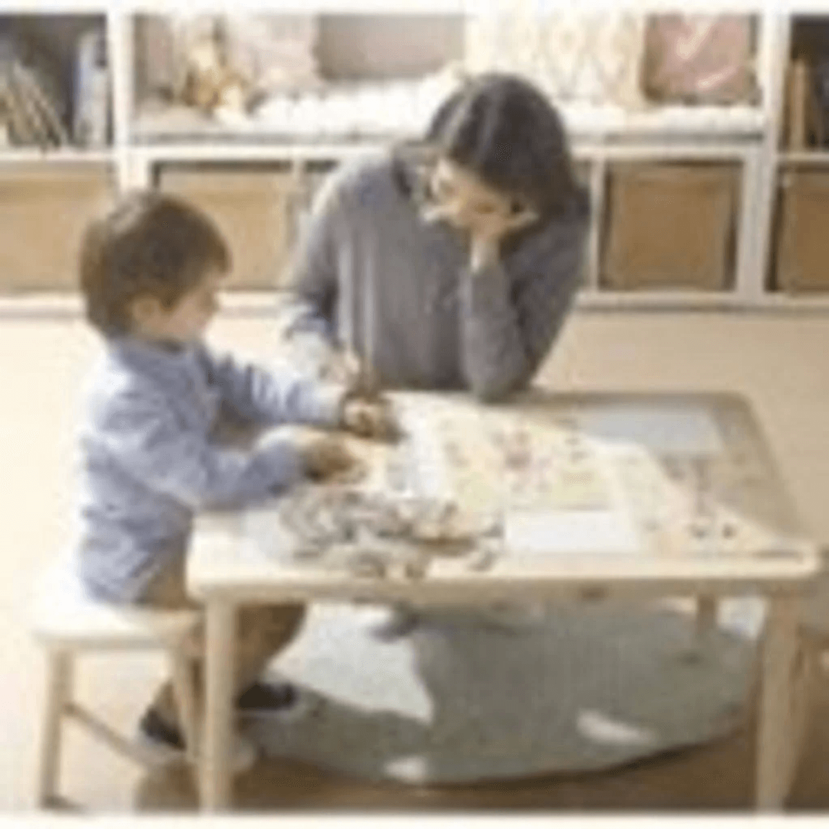 Eine Frau und ein Junge sitzen an einem Holztisch und spielen zusammen in einem hellen Zimmer.