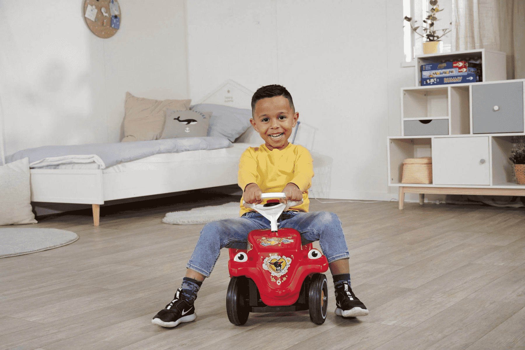 Un niño feliz monta en un coche de juguete rojo en su habitación.
