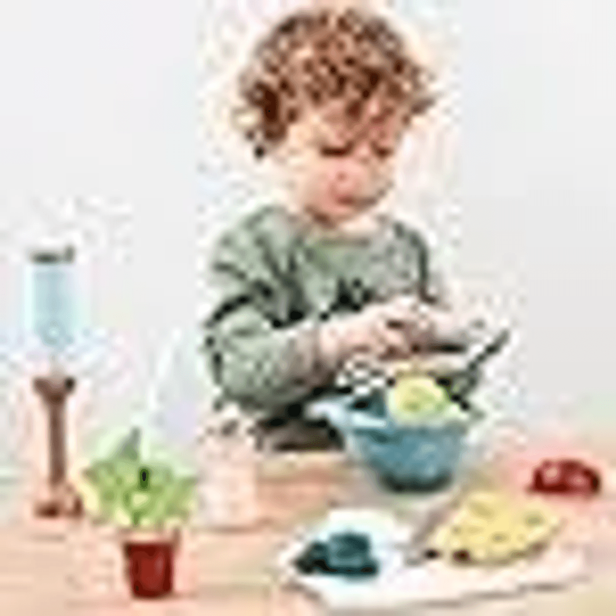 Niño pequeño con cabello rizado jugando con comida y utensilios de cocina en una mesa.