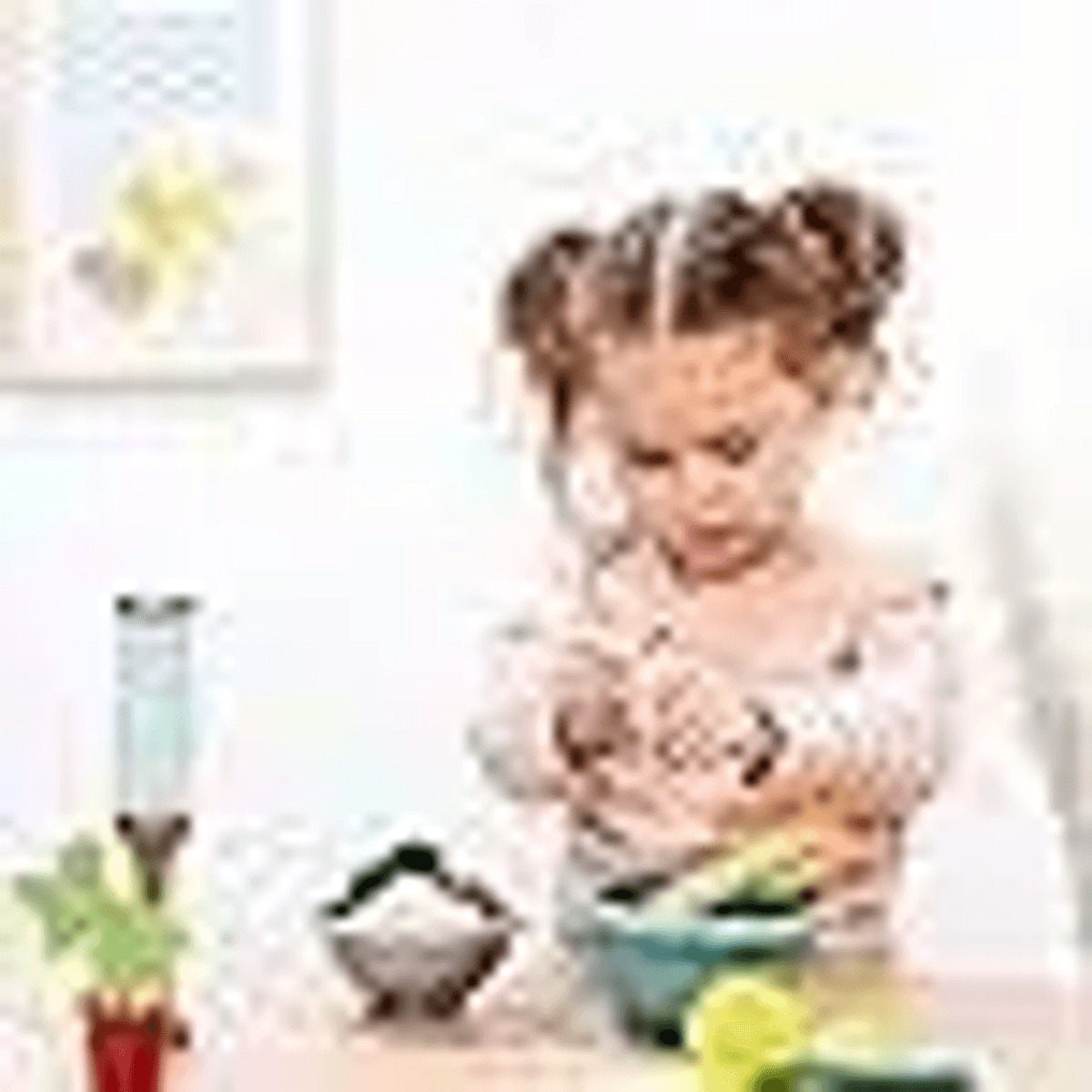 Una niña pequeña con coletas prepara comida en una cocina luminosa.