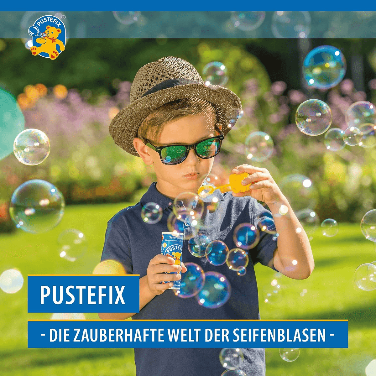 Un niño con sombrero y gafas de sol sopla pompas de jabón en el jardín. Logotipo y texto de Pustefix.