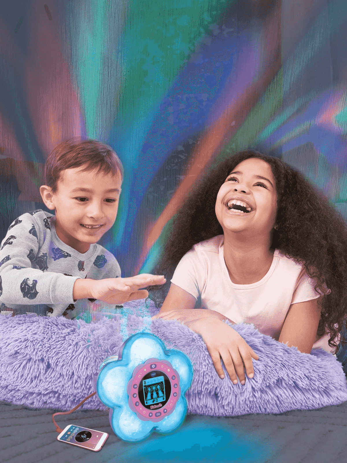 Dos niños sonrientes cerca de un proyector en forma de flor sobre una manta.