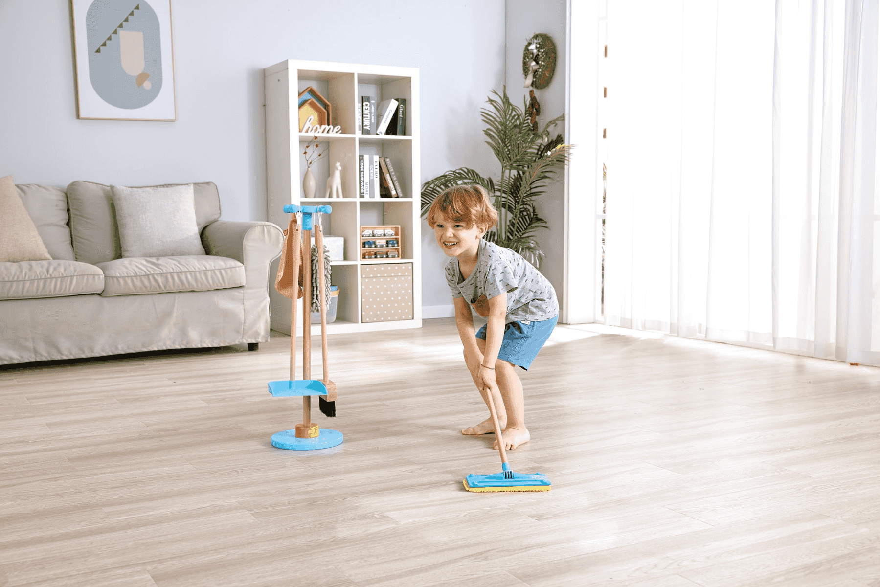 Un niño pequeño trapea alegremente el suelo de madera en una sala moderna y luminosa.