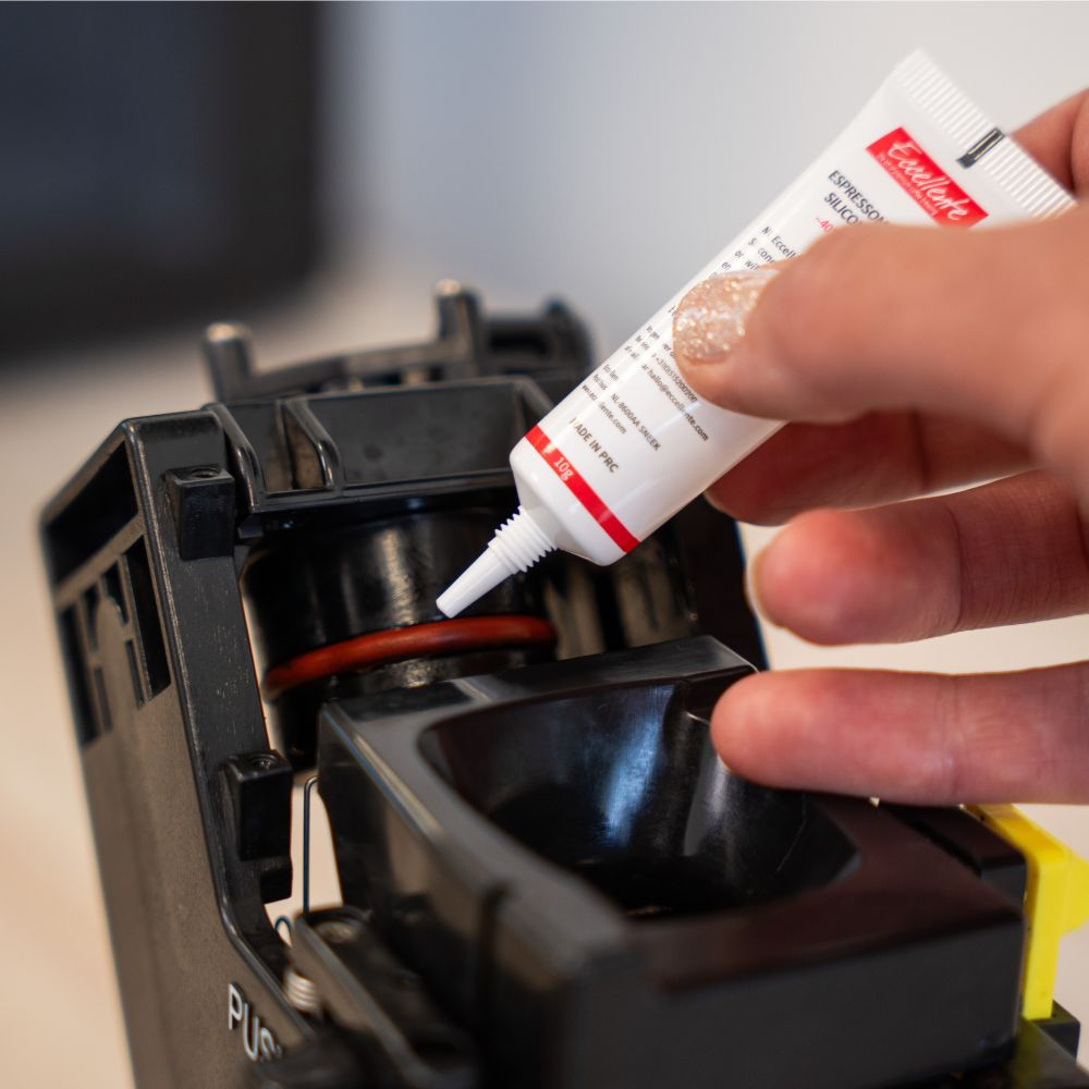 Een hand brengt siliconenvet aan op de rode ring van een koffiezetapparaat.