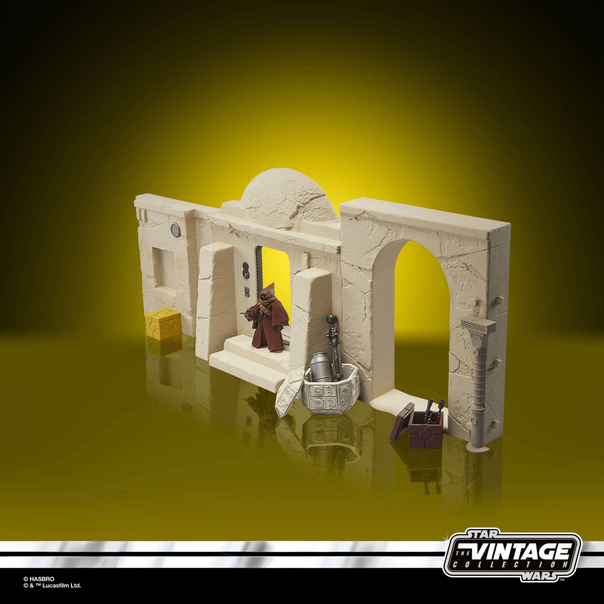 Una figura de acción de Star Wars con túnica marrón frente a una fachada de edificio arenosa con arcos y accesorios.