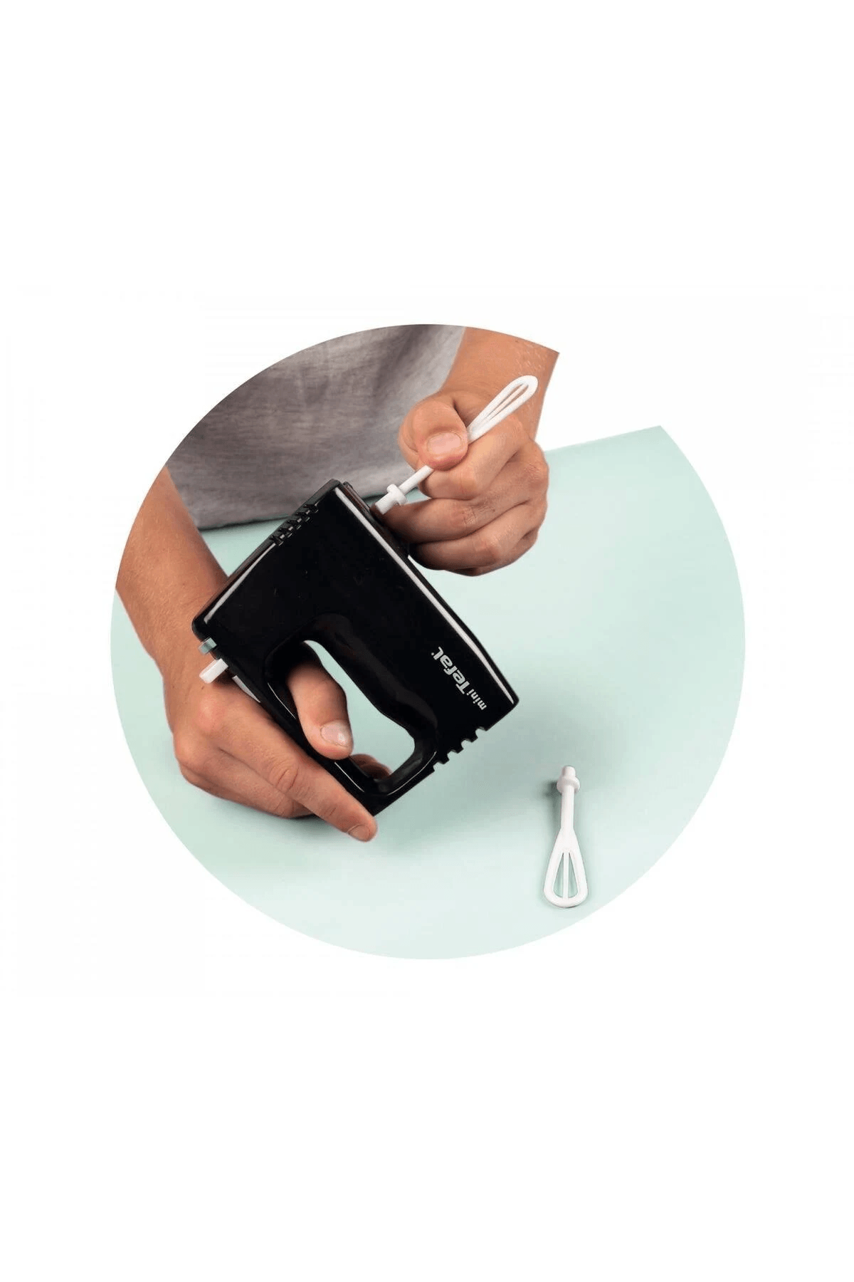 Una persona insertando una varilla blanca en una batidora manual negra Mini Tefal sobre fondo azul claro.
