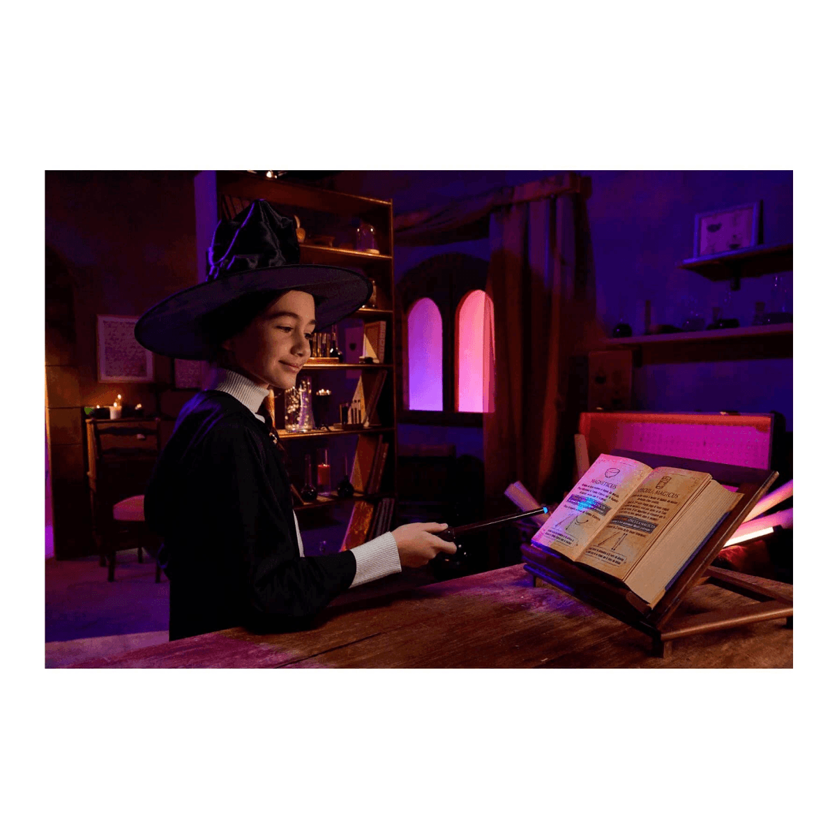 Una niña con sombrero de bruja usa una varita para iluminar un libro abierto en una habitación oscura.