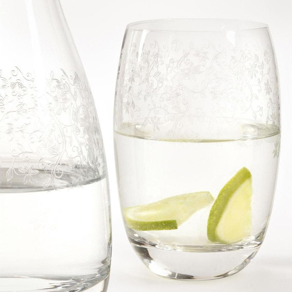 Ein graviertes Glas und eine Karaffe mit Wasser und Gurkenscheiben vor weißem Hintergrund.