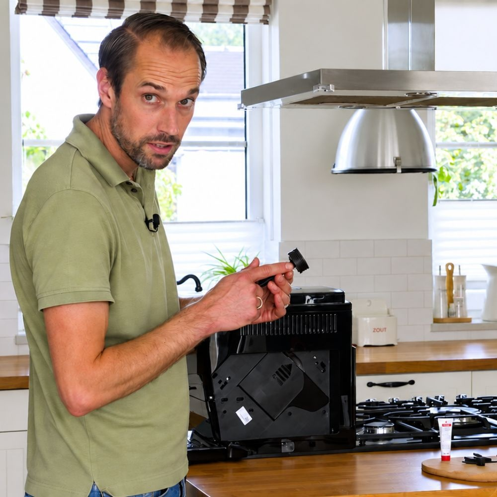 A man in a green polo shirt stands in a kitchen next to a coffee machine.