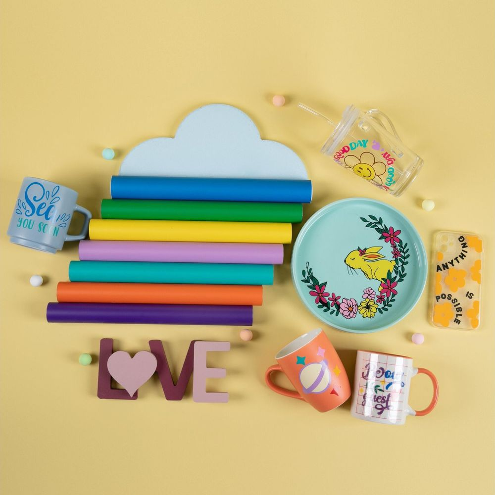 Bunte Bastelmaterialien und Tassen mit niedlichen Motiven auf gelbem Hintergrund angeordnet.