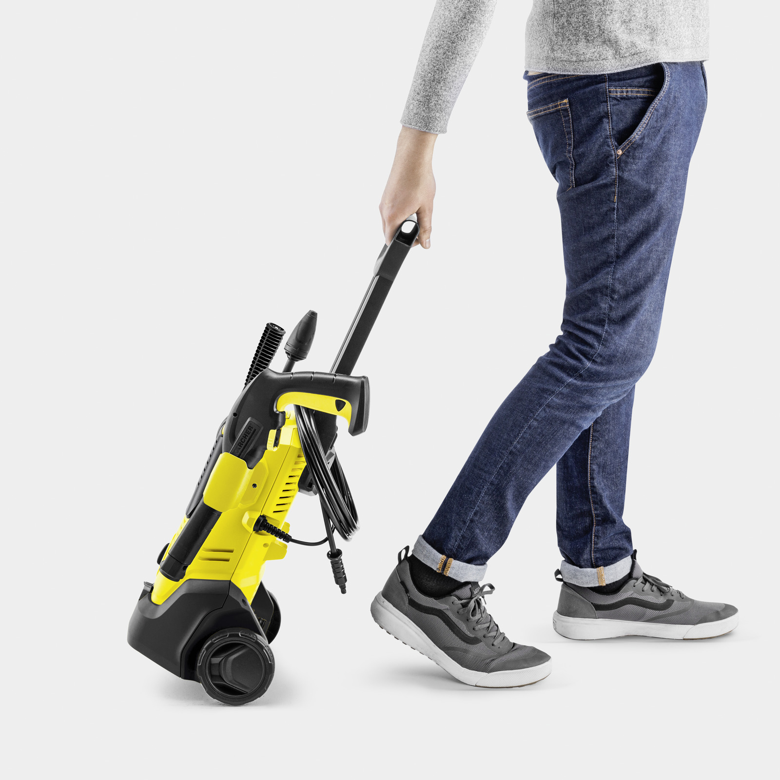 Une personne en jean et baskets tire un nettoyeur haute pression jaune et noir.