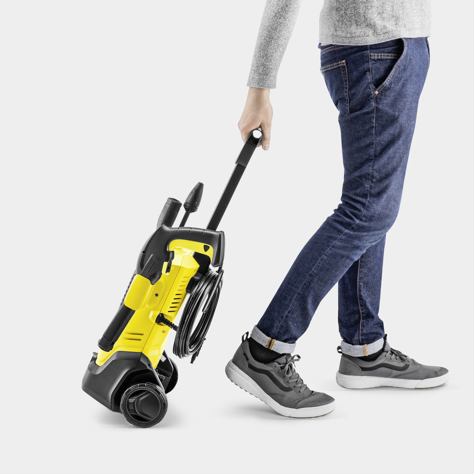 Une personne de profil tire un nettoyeur haute pression Kärcher jaune et noir sur une surface blanche.