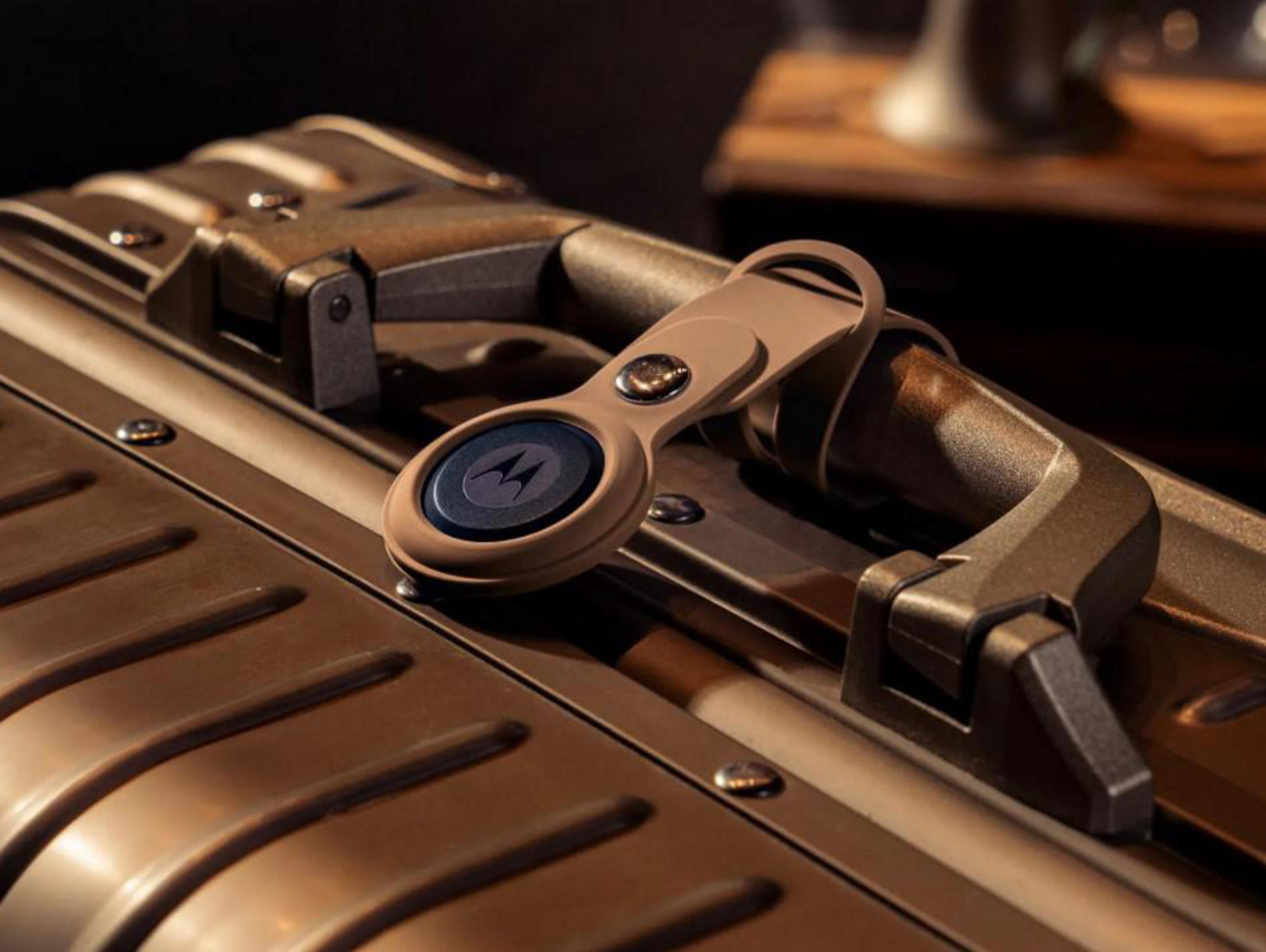 Un rastreador Motorola en una funda de cuero marrón claro está sujeto al asa de una maleta metálica.