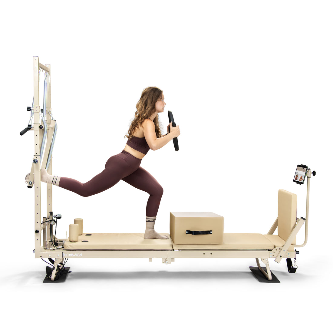 Una mujer en ropa deportiva hace ejercicios de pilates en una máquina reformer, sosteniendo un disco de peso.