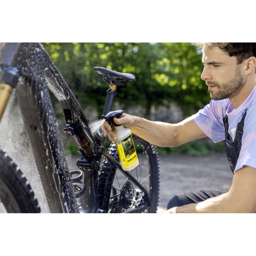 Ein Mann sprüht Reiniger auf sein schlammiges Mountainbike im Freien.