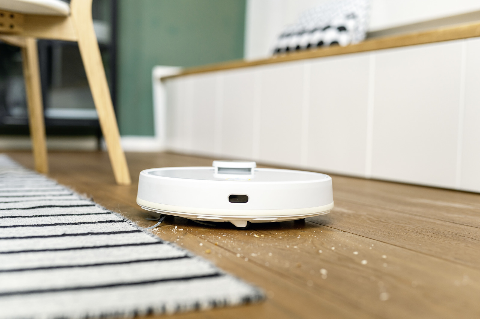 Un robot aspirador blanco limpia un suelo de madera en una habitación moderna con una alfombra.