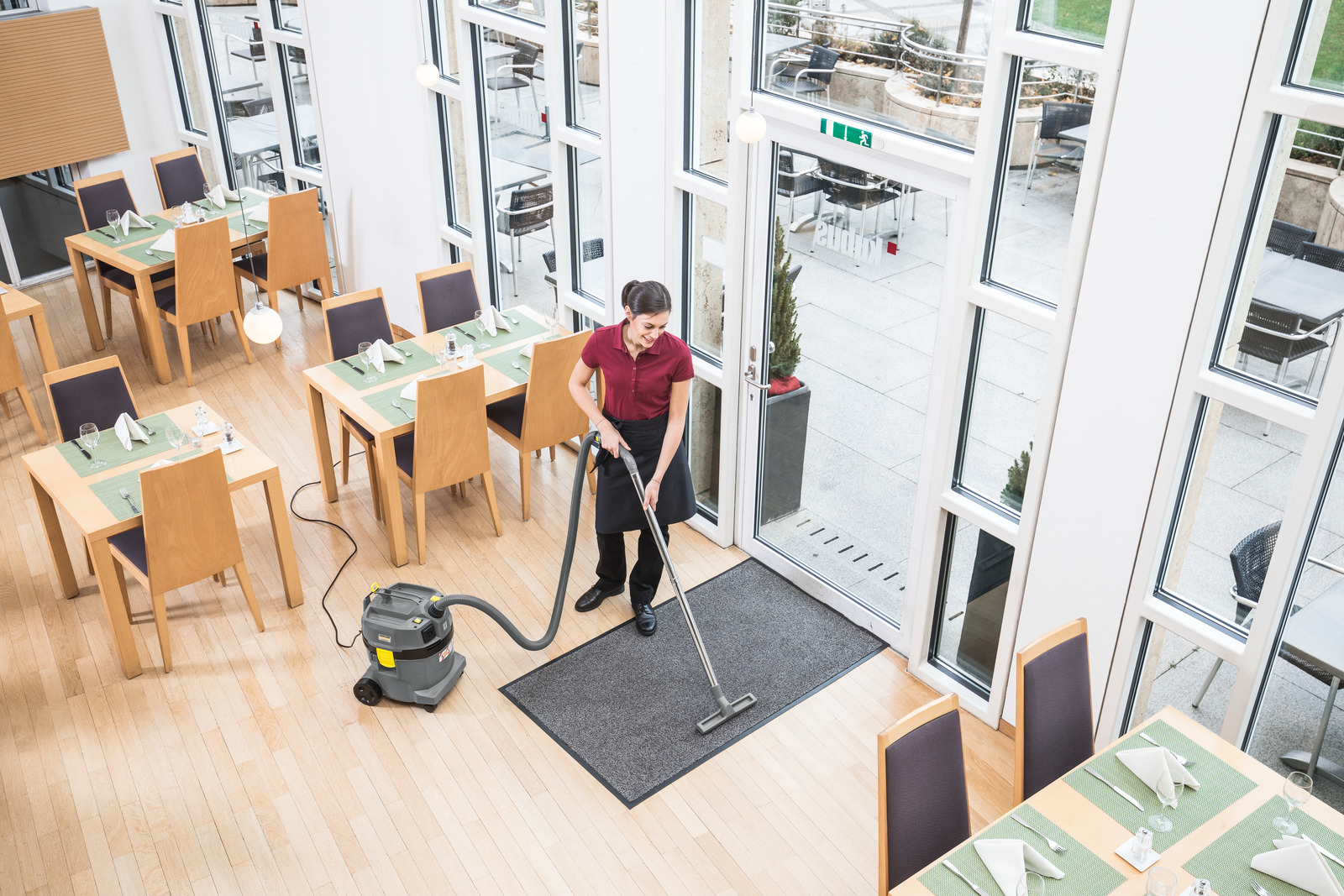 Una donna in abiti da lavoro passa l'aspirapolvere all'ingresso di un ristorante luminoso.