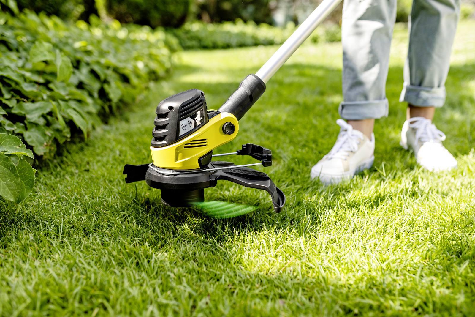 Eine Person benutzt einen gelb-schwarzen Rasentrimmer auf einem grünen Rasen mit Garten.