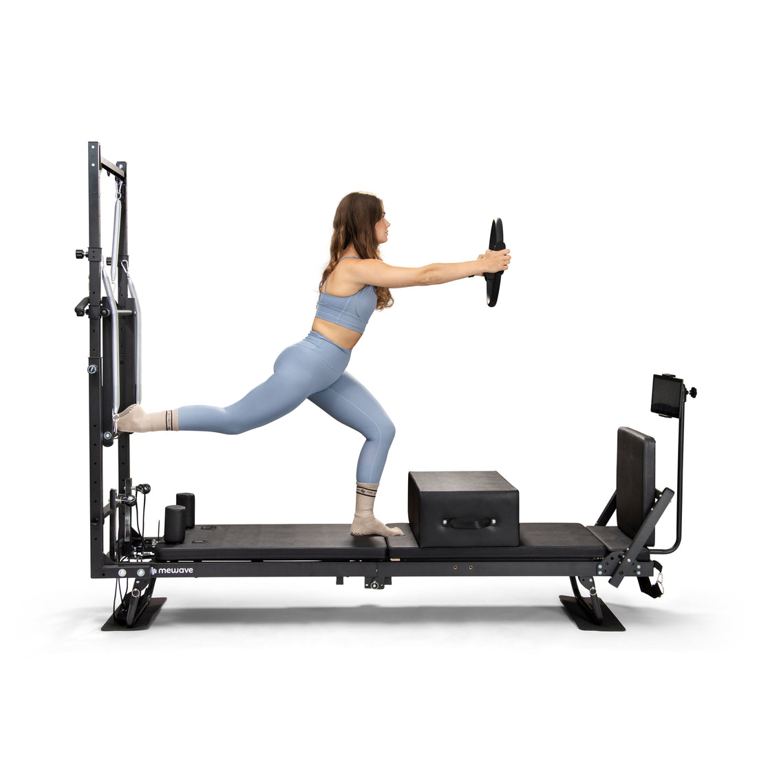 Una mujer con ropa de deporte azul hace ejercicio en una máquina de pilates negra, sosteniendo un aro.