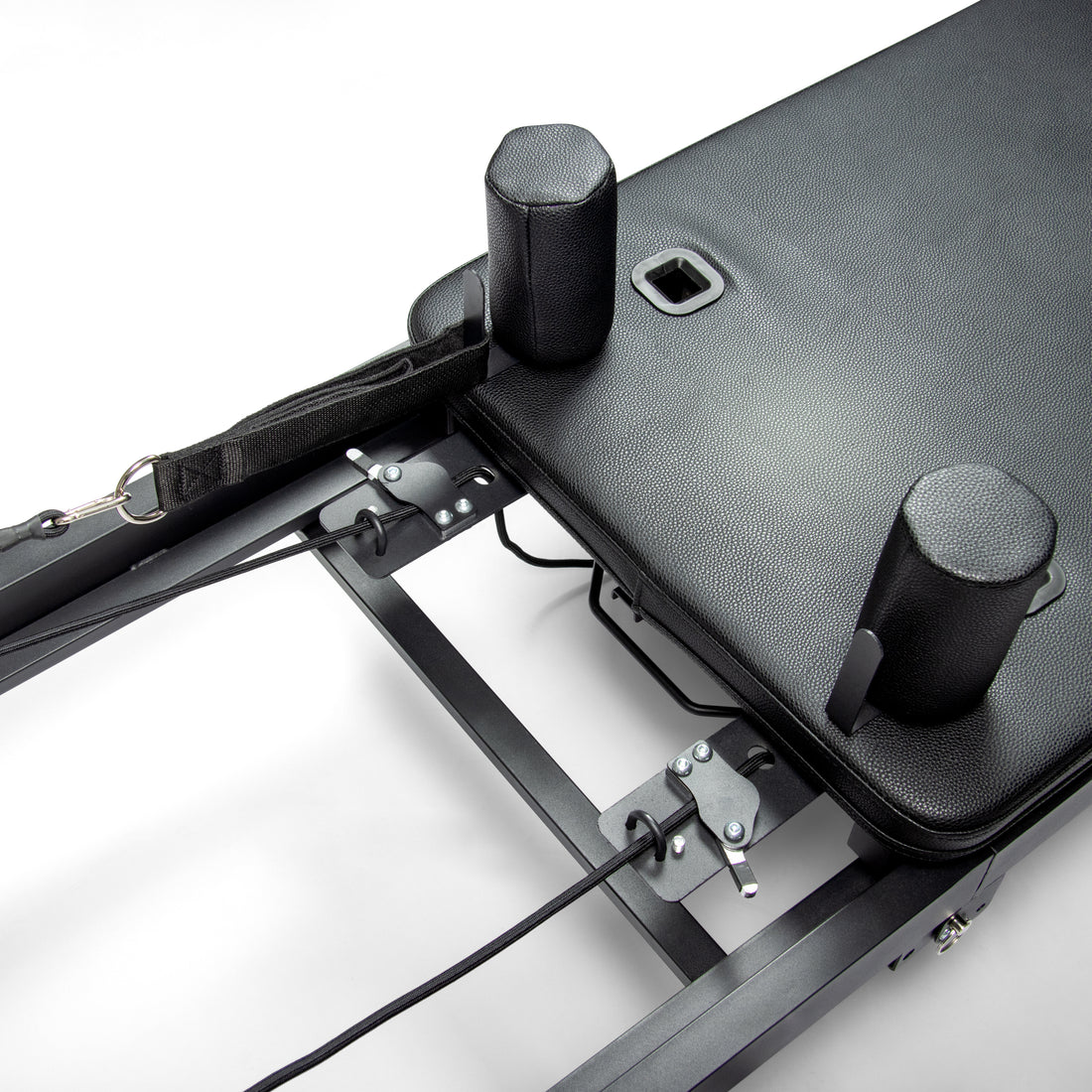 Primer plano de un reformador de pilates negro con carro acolchado, soportes para hombros y cuerdas ajustables.
