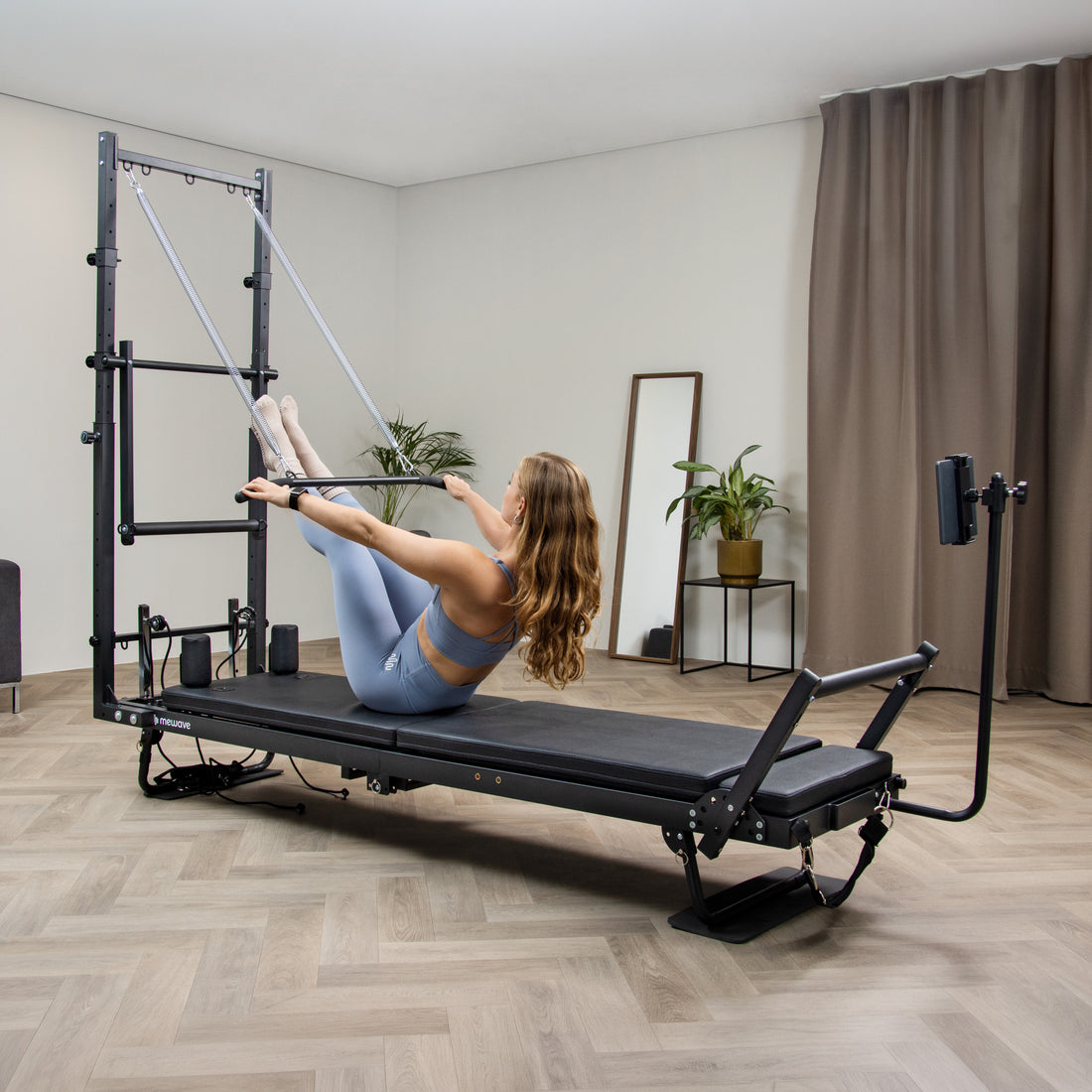 Una mujer con ropa deportiva azul hace ejercicio en un reformador de pilates.