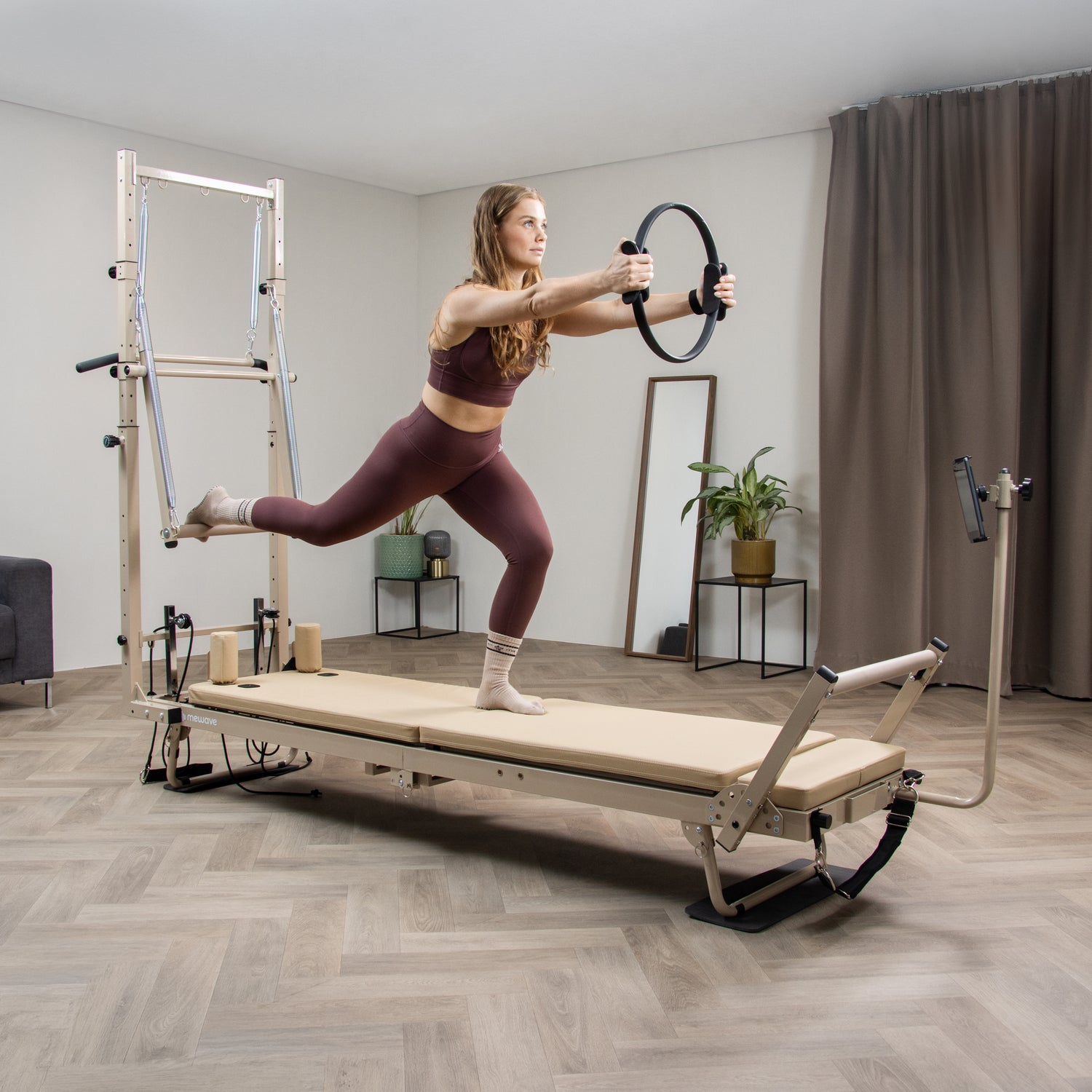 Una mujer en ropa deportiva burdeos hace ejercicio en un reformador de Pilates, sosteniendo un anillo negro.