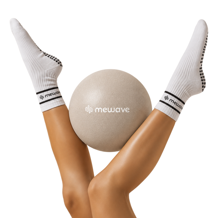 Piernas con calcetines blancos antideslizantes Mewave sostienen una pelota gris.